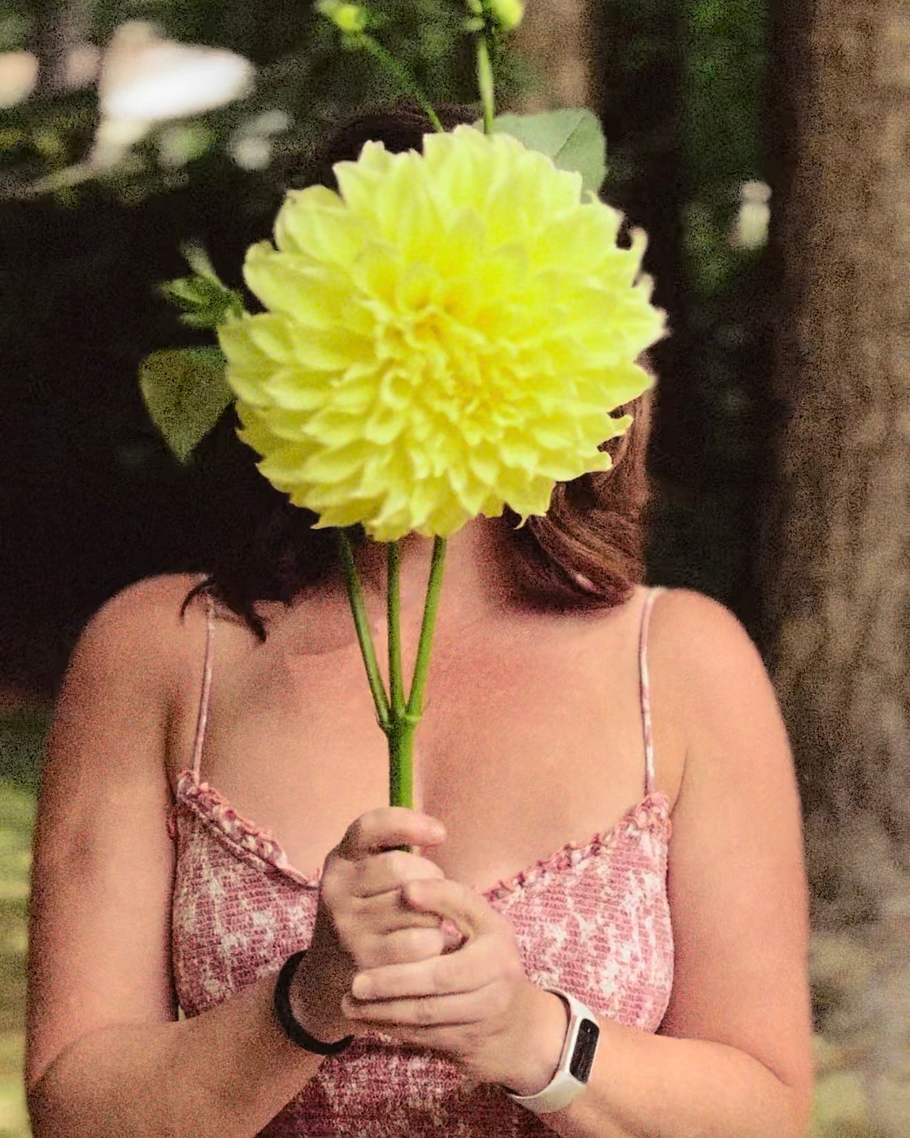 Person holding a large green flower in front of their face outdoors.