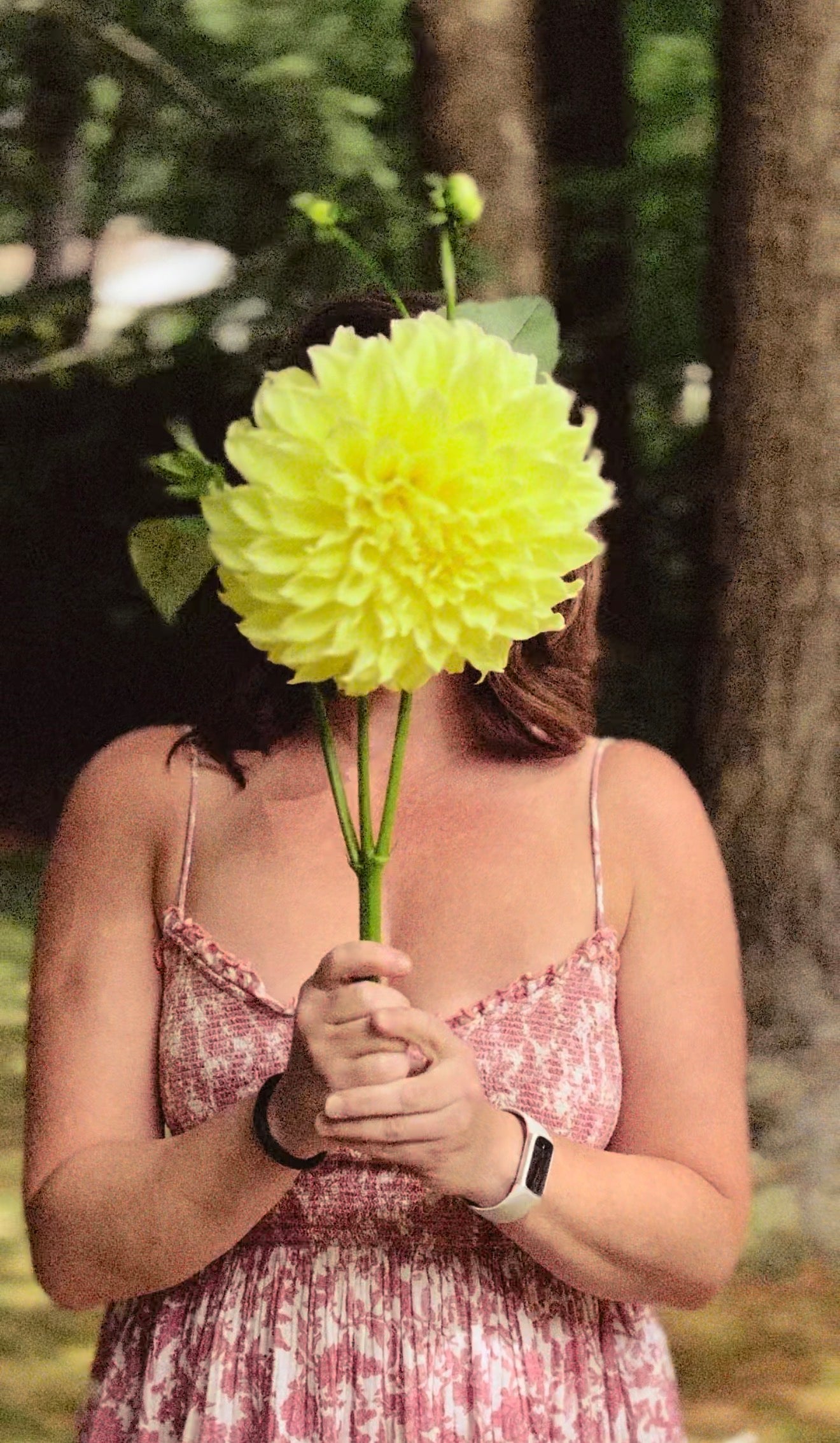 Person holding a large green flower in front of their face outdoors.