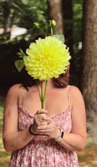 Person holding a large green flower in front of their face outdoors.