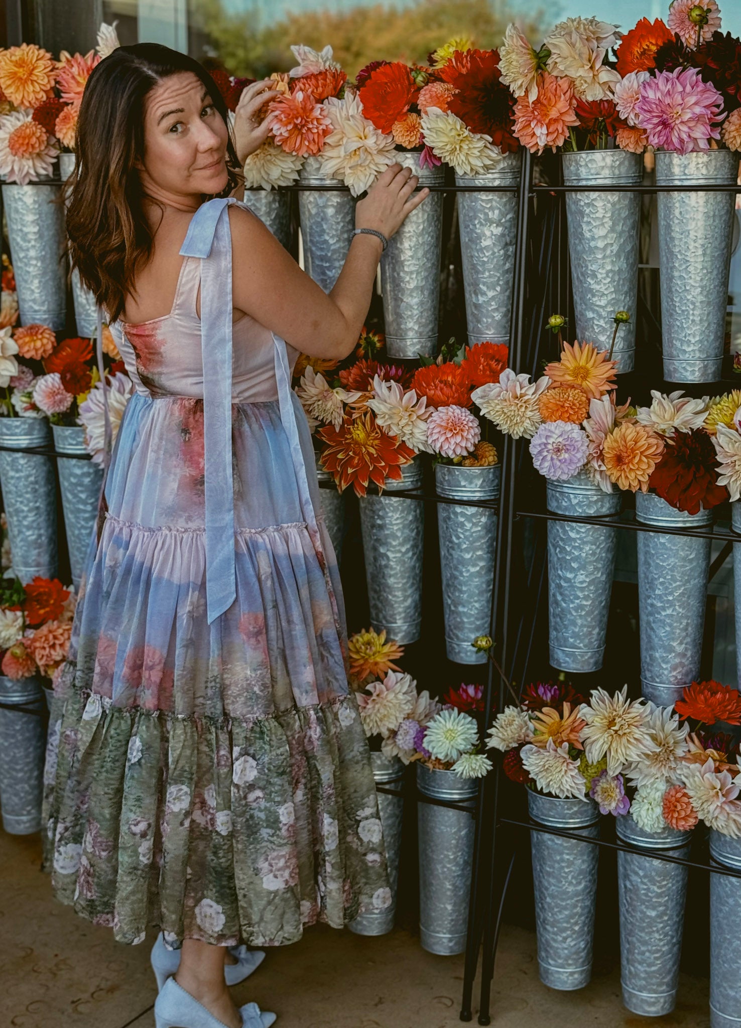 shannonin a floral dress standing among flower arrangements in metal vases.